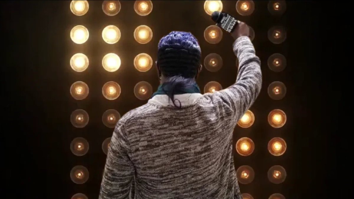 Ms. Darkchild performing on stage, microphone raised against a wall of lights